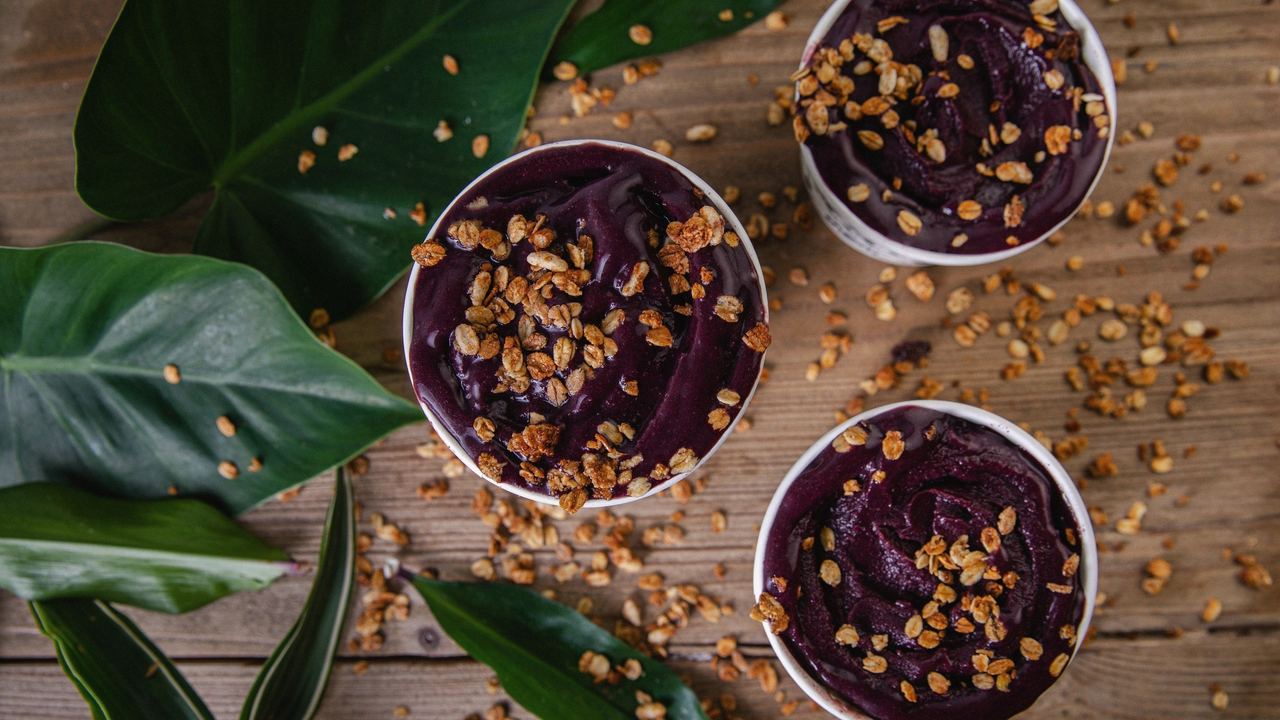 Açaí cream bowls topped with granola, on wood among tropical leaves